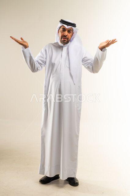 التردد وعدم الثقة بخصوص أمر معين، بورتريه لشاب عربي خليجي كويتي يرتدي الثوب التقليدي والغترة يقف و يرفع كفيه للاعلى بإيماءات عدم التأكد،  النظر الى الكاميرا بتعابير الحيرة وعدم المعرفة، صورة الجسم بالطول الكامل, خلفية بيضاء