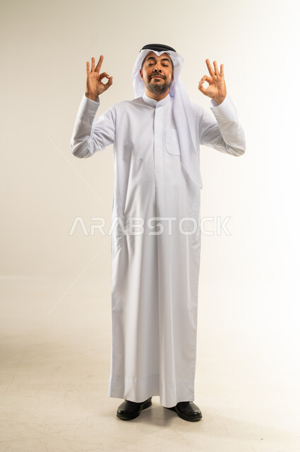 التعبير عن الجودة والاتقان، البشاشة والشعور بالرضا, الموافقة والقبول والنصيحة، بورتريه لرجل عربي خليجي كويتي مبتسم يرتدي الثوب التقليدي والغترة يقوم  برفع يديه بحركات دائرية بإيماءات الجودة والامتياز والتميز، صورة الجسم بالطول الكامل, خلفية بيضاء