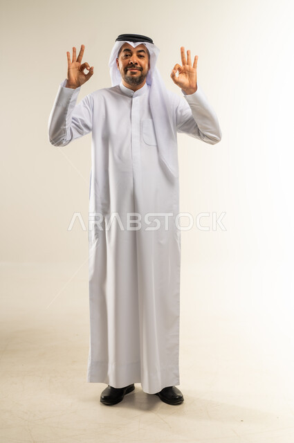 التعبير عن الجودة والاتقان، البشاشة والشعور بالرضا, الموافقة والقبول والنصيحة، بورتريه لرجل عربي خليجي كويتي مبتسم يرتدي الثوب التقليدي والغترة يقوم  برفع يديه بحركات دائرية بإيماءات الجودة والامتياز والتميز، صورة الجسم بالطول الكامل, خلفية بيضاء