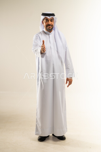 إلقاء التحية والسلام، مد كف يد نحو الأمام للمصافحة،  مفهوم التقدير والاحترام، بورتريه لرجل عربي خليجي كويتي مبتسم يرتدي الثوب التقليدي والغتره ينظر إلى الكاميرا بإيماءات السعادة والسرور، الأناقة والوسامة والرجولة، الجسم بالطول الكامل، خلفية بيضاء