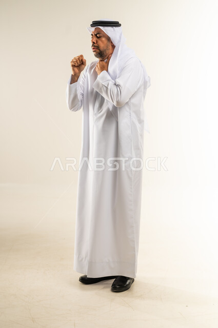 الكحة والتهاب الحلق، الحاجة لزيارة الطبيب وأخذ العلاج المناسب، إيماءات الإرهاق والتعب الشديد، الإصابة بالأنفلونزا ونزلات البرد، بورتريه لرجل عربي خليجي كويتي يرتدي الغترة والثوب التقليدي يضع يده أمام فمه ويقوم بالسعال, الجسم بالطول الكامل، خلفية بيضاء