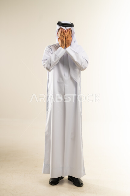 الشعور بالخجل والإحراج، إغماض العينين وعدم الرغبة بالرؤية، البكاء ومشاعر الحزن، التعرض لصدمة وعدم التصديق، بورتريه لرجل عربي خليجي كويتي يرتدي الثوب التقليدي والغتره يغطي وجهه بيديه، الجسم بالطول الكامل، خلفية بيضاء