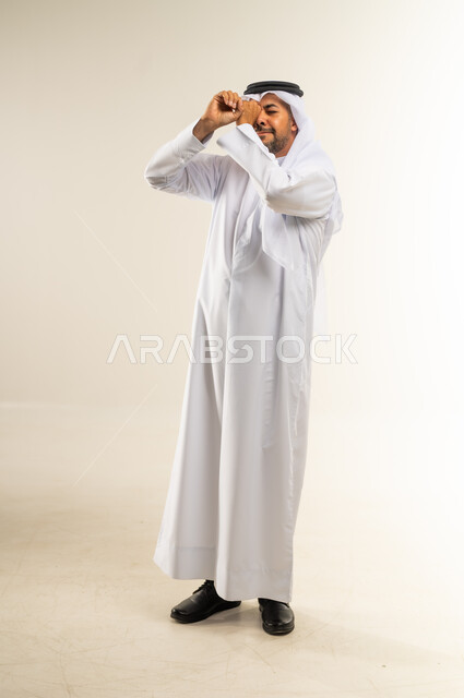حب الاكتشاف والمعرفة والمغامرة، محاولة تقريب الأشياء البعيدة، التخطيط للأهداف والطموحات المستقبلية، التركيز على شيء ما، بورتريه لرجل عربي خليجي كويتي يرتدي الثوب التقليدي والغترة يضع يده على عينه بشكل عدسة بإيماءات البحث، الجسم بالطول الكامل، خلفية بيضاء
