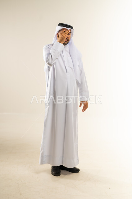 تذكر شيء ما بشكل مفاجئ، الشعور بالخجل والإحراج، محاولة استراق النظر، البكاء ومشاعر الحزن، إغماض العينين وعدم الرغبة بالرؤية، التعرض لصدمة وعدم التصديق، بورتريه لرجل عربي خليجي كويتي يرتدي الثوب التقليدي والغتره يغطي وجهه بيده، الجسم بالطول الكامل، خلفية بيضاء