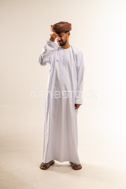 الاحساس بالشقيقية والصداع النصفي, الشعور بالإرهاق وفقدان التركيز, الاجهاد والضغط النفسي, بورتريه لرجل عربي خليجي عماني يرتدي الدشداشه والعمامة يضع يديه على رأسه ويغمض عينيه بإيماءات وجع في الدماغ والرأس الشديد, صورة الجسم بالطول الكامل, خلفية بيضاء