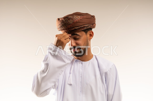 الاحساس بالشقيقية والصداع النصفي, الشعور بالإرهاق وفقدان التركيز, الاجهاد والضغط النفسي, بورتريه لرجل عربي خليجي عماني يرتدي الدشداشه والعمامة يضع يديه على رأسه ويغمض عينيه بإيماءات وجع في الدماغ والرأس الشديد خلفية بيضاء
