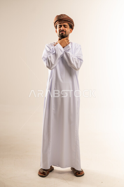 الاحساس بالاختناق وعدم القدرة على التنفس، الشعور بآلام في الحلق، أمراض البلعوم والتهاب اللوزتين، بورتريه لرجل عربي خليجي عماني يرتدي الدشداشه والعمامة يضع يديه حول عنقه بإيماءات المعاناة والتوجع، الجسم بالطول الكامل، خلفية بيضاء