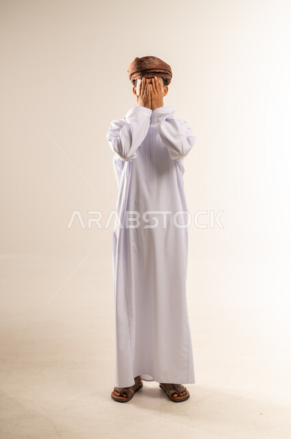 إغماض العينين وعدم الرغبة بالرؤية، الشعور بالخجل والإحراج، البكاء ومشاعر الحزن، التعرض لصدمة وعدم التصديق، بورتريه لرجل عربي خليجي عماني يرتدي الدشداشة والعمامة يغطي وجهه بيديه، الجسم بالطول الكامل، خلفية بيضاء