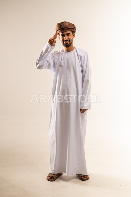 إلقاء التحية والسلام، الأناقة والوسامة والرجولة، مفهوم التقدير والاحترام، بورتريه لرجل عربي خليجي عماني مبتسم يرتدي الدشداشة والعمامة ينظر إلى الكاميرا بإيماءات السعادة والسرور، الوقوف باستقامة بتعابير الثقة بالنفس، الجسم بالطول الكامل، خلفية بيضاء