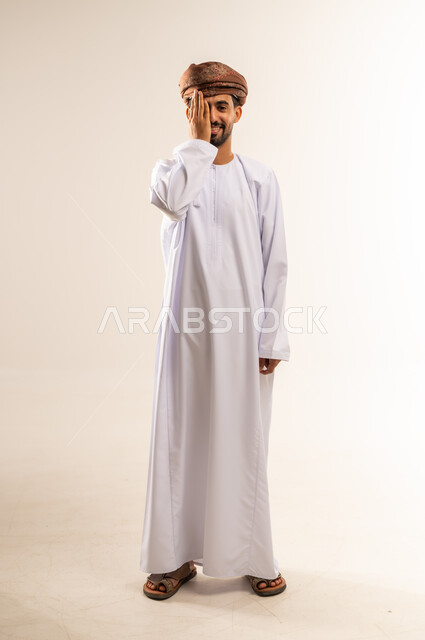 وضع اليد على العين وتغطيها، التهاب واحمرار العيون والحاجة لزيارة الطبيب، ضعف النظر وتشوش الرؤية، التعرض لأذية في الشبكية، بورتريه لرجل عربي خليجي عماني يرتدي الدشداشة والعمامة يعاني من مشاكل صحية في عينه، الجسم بالطول الكامل، خلفية بيضاء