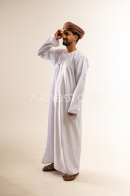مفهوم التخطيط و الرؤية المستقبلية، بورتريه من الجانب لشاب عربي خليجي عماني مبتسم يرتدي الدشداشة و العمامة يضع يده على عينيه بشكل عدسة دائرية بإيماءات البحث والاستكشاف، صورة الجسم بالطول الكامل, خلفية بيضاء