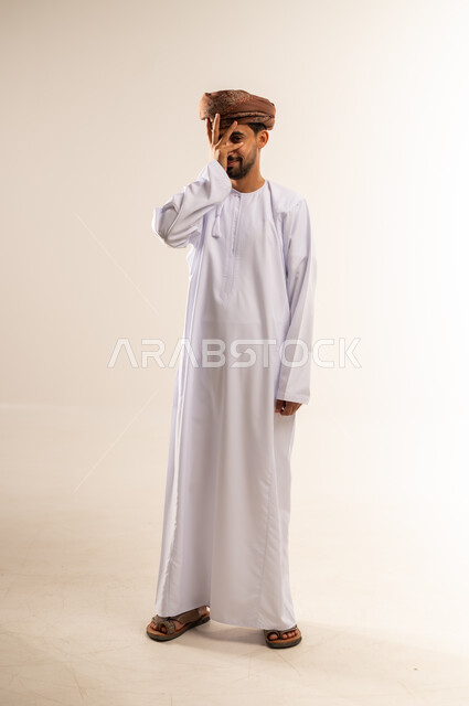 الشعور بالخجل والإحراج، محاولة استراق النظر، البكاء ومشاعر الحزن، إغماض العينين وعدم الرغبة بالرؤية، التعرض لصدمة وعدم التصديق، بورتريه لرجل عربي خليجي عماني يرتدي الدشداشه والعمامة يغطي وجهه بيده، الجسم بالطول الكامل، خلفية بيضاء