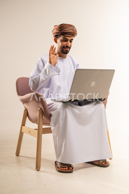 عقد إجتماع عمل عبر الإنترنت، مناقشة إستراتيجية المشروع, إدارة شؤون الأعمال وتنظيمها، استخدام التقنيات الحديثة المتطورة، بورتريه لرجل عربي خليجي عماني يرتدي الدشداشة والعمامة يجلس على كرسي مريح يقوم بإجراء مكالمة فيديو من خلال الحاسب المحمول، خلفية بيضاء