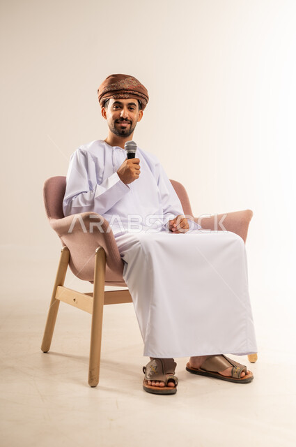 تبادل الحوار والاستفادة من الخبرات، إلقاء المحاضرات وإقامة الندوات، بورتريه لشاب عربي خليجي عماني يرتدي الدشداشة والعمامة يحمل بيده المايكروفون ينظر الى الكاميرا بتعابير السرور، العمل في تقديم الفقرات والبرامج الفنية الترفيهية، خلفية بيضاء
