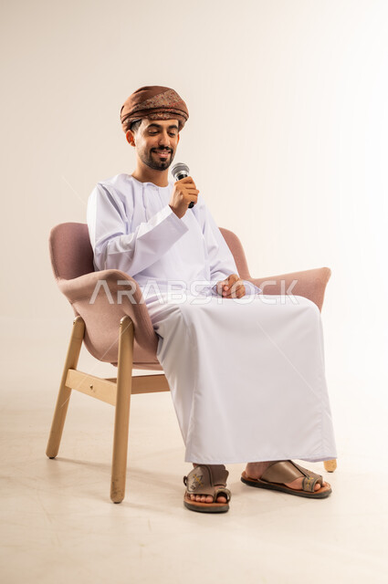 إلقاء المحاضرات وإقامة الندوات، تبادل الحوار والاستفادة من الخبرات، بورتريه لشاب عربي خليجي عماني يرتدي الدشداشة والعمامة يحمل بيده المايكروفون، العمل في تقديم الفقرات والبرامج الفنية الترفيهية، خلفية بيضاء