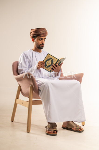 تلاوة وقراءة القرآن الكريم وتدبر معانيه، بورتريه لرجل عربي خليجي عماني يرتدي الدشداشة والعمامة يحمل بيده المصحف الشريف، الإكثار من ذكر الله تعالى، الشعور بالخشوع والطمأنينة، خلفية بيضاء