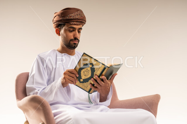 الإكثار من ذكر الله تعالى، تلاوة وقراءة القرآن الكريم وتدبر معانيه، بورتريه مقرب لرجل عربي خليجي عماني يرتدي الدشداشة والعمامة يحمل بيده المصحف الشريف، الشعور بالخشوع والطمأنينة، خلفية بيضاء