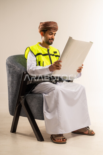 إيماءات البهجة والسرور، مهن ووظائف هندسية، التدقيق والإشراف على مخططات المشروع، بورتريه لرجل عربي خليجي عماني يرتدي سترة الحماية الخاصة بالعمل يجلس على كرسي مريح يمسك بيده مخطط هندسي ينظر لمكان ما بتعابير الشرود، خلفية بيضاء