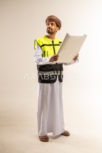 التدقيق والإشراف على مخططات المشروع، إيماءات البهجة والسرور، مهن ووظائف هندسية، بورتريه لرجل عربي خليجي عماني يرتدي سترة الحماية الخاصة بالعمل يمسك بيده مخطط هندسي ينظر لمكان ما بتعابير الشرود، صورة لكامل الجسم، خلفية بيضاء