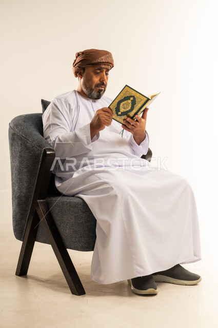 تلاوة وقراءة القرآن الكريم وتدبر معانيه، بورتريه لرجل عربي خليجي عماني يرتدي الدشداشة والعمامة يحمل بيده المصحف الشريف، الإكثار من ذكر الله تعالى، الشعور بالخشوع والطمأنينة، خلفية بيضاء