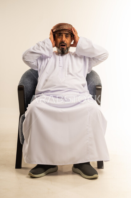 الشعور بالدهشة والصدمة والذهول, التفاجؤ من شيء ما، بورتريه لرجل عربي خليجي عماني يرتدي الدشداشة والعمامة يضع يديه على رأسه بإيماءات التعجب، خلفية بيضاء