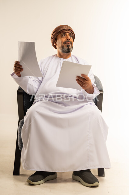اعداد التقارير الخاصة بالعمل، بورتريه لرجل عربي خليجي عماني يرتدي الدشداشة والعمامة يحمل بيده مجموعة من الاوراق، مراجعة ومتابعة الخطط والمشاريع المكتبية، التدقيق في قراءة الملاحظات، خلفية بيضاء