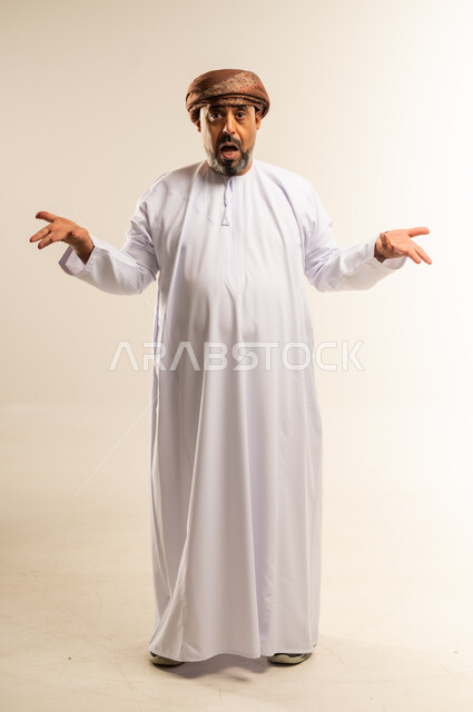 عدم التاكد والقدرة على اتخاذ القرار، التردد بشأن أمر معين، بورتريه لرجل عربي خليجي عماني يرتدي الدشداشة والعمامة يرفع كفيه نحو الأعلى بتعابير الحيرة، النظر إلى الكاميرا بإيماءات الاستغراب، صورة الجسم بالطول الكامل، خلفية بيضاء