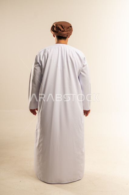مفهوم الرجولة والوقار، الاهتمام بالمظهر الخارجي، بورتريه من الخلف لرجل عربي خليجي عماني يرتدي الدشداشة والعمامة يقف باستقامة، صورة الجسم بالطول الكامل، خلفية بيضاء