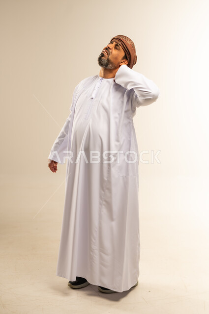طلب المساعده والحاجه للعلاج، التهاب العضلات والمفاصل، بورتريه لرجل عربي خليجي عماني يرتدي الدشداشة والعمامة يضع يده على رقبته بايماءات الألم والتعب والأرهاق، حالة اسعافية طارئة، الأوجاع والآلام العصبية والعضلية، صورة لكامل الجسم، خلفيةبيضاء