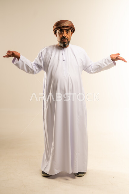 عدم التاكد والقدرة على اتخاذ القرار، التردد بشأن أمر معين، بورتريه لرجل عربي خليجي عماني يرتدي الدشداشة والعمامة يرفع كفيه نحو الأعلى بتعابير الحيرة، النظر إلى الكاميرا بإيماءات الاستغراب، صورة الجسم بالطول الكامل، خلفية بيضاء