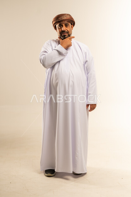 Finding a solution to a problem, contemplation and planning for the future, portrait of an Arab Gulf Omani man wearing a dishdasha and turban, putting his hand on his chin with gestures of thinking and concentration, expressions of absent-mindedness and contemplation, full body image, white background