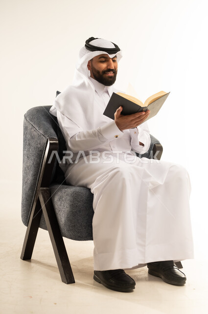 زيادة الذخيرة الفكرية، قضاء أوقات الفراغ بشكل مفيد، تنمية المهارات وتوسيع المعارف والأفكار، الاستمتاع بقراءة الكتب والقصص والروايات، بورتريه لشاب عربي خليجي قطري يرتدي الثوب التقليدي والغترة يجلس على كرسي ويمسك بيديه كتاب، خلفية بيضاء