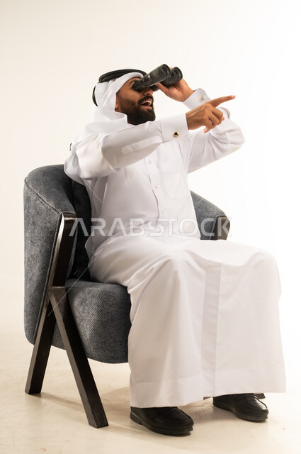 رؤية الاشياء البعيدة عبر المنظار، حب المغامرة والاستكشاف، بورتريه لرجل عربي خليجي قطري مبتسم يرتدي الثوب التقليدي والغترة يجلس على كرسي مريح ينظر من خلال منظار الرؤية ويشير باصبع السبابة لمكان ما, التخطيط المستقبلي للأهداف والطموحات، خلفية بيضاء