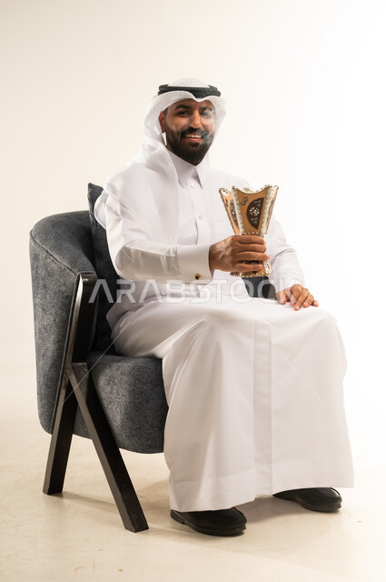 Following authentic Arab customs and traditions, using oud wood on holidays and happy occasions, incense burning and using perfumes and fragrances, portrait of a Qatari Gulf Arab man wearing traditional thobe and ghutra sitting on a chair and holding incense burner in his hand with gestures of joy and happiness, white background