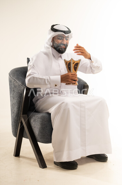 استخدام خشب العود  في الأعياد والمناسبات السعيدة، اتباع العادات والتقاليد العربية الأصيلة، التبخير واستعمال العطور والمطيبات، بورتريه لرجل عربي خليجي قطري يرتدي الثوب التقليدي والغترة يجلس على كرسي ويمسك بيده المبخرة بايماءات الفرح والسرور، خلفية بيضاء
