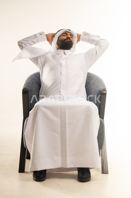الشعور بالتعب والحاجة إلى الراحة، مفهوم الاسترخاء والاستمتاع بالأجواء الهادئة، بورتريه لشاب عربي خليجي قطري يرتدي االثوب التقليدي والغترة يجلس على كرسي مريح ويضع يديه خلف رأسه للنوم، خلفية بيضاء