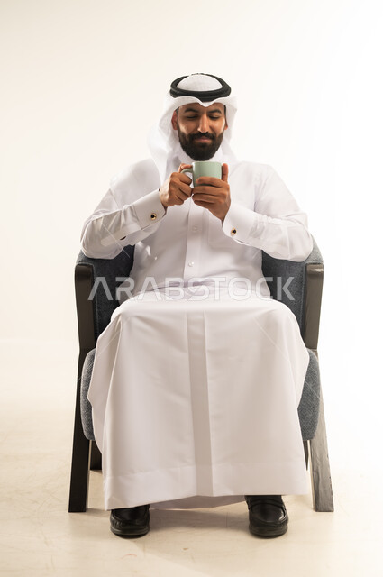 الحيوية والنشاط عند شرب الكافيين، الاستمتاع والاحساس بالدفء عند تناول المشروبات الساخنة، بورتريه لرجل عربي خليجي قطري يرتدي الثوب التقليدي والغترة يحمل بيده كوب القهوة، خلفية بيضاء