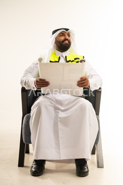 Concept of engineering and architectural construction, working in the engineering sector, portrait of a Qatari Gulf Arab man wearing a thobe with a protective vest and a ghutra sitting on a comfortable chair holding construction plans in his hands, looking somewhere above with expressions of pride and pleasure, project management and follow-up, white background