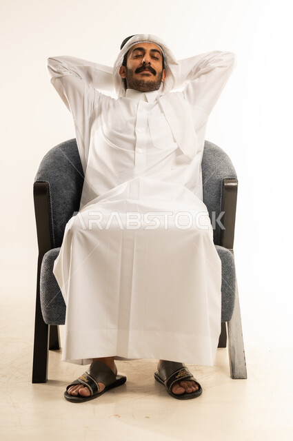 الشعور بالتعب والحاجة إلى الراحة، مفهوم الاسترخاء والاستمتاع بالأجواء الهادئة، بورتريه لرجل عربي خليجي قطري يرتدي االثوب التقليدي والغترة يجلس على كرسي مريح ويضع يديه خلف رأسه للنوم، الإحساس بالكسل والخمول، خلفية بيضاء