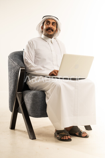 دمج والتكنولوجيا في الحياة العملية، مفهوم التوظيف أونلاين، العمل عن بعد عبر الانترنت باستخدام الحاسب المحمول, بورتريه لرجل عربي خليجي قطري يرتدي الثوب التقليدي والغترة يجلس على كرسي مريح يضع يديه على جهاز اللابتوب، النظر الى مكان ما بتعابير التفكير، خلفية بيضاء