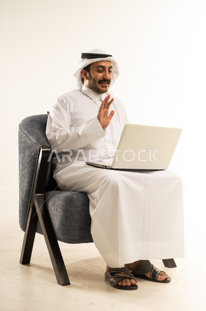 ايماءات الترحيب والتحية والسلام، دمج التقنيات الحديثة في الحياة اليومية، التواصل مع الاهل والاصدقاء عبر الانترنت, بورتريه لرجل عربي خليجي قطري يرتدي الثوب التقليدي والغترة يجلس على كرسي مريح يقوم بإجراء مكالمة فيديو عبر جهاز اللابتوب، خلفية بيضاء