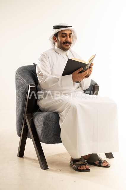تنمية المهارات وتوسيع المعارف والأفكار، الاستمتاع بقراءة الكتب والقصص والروايات، بورتريه لرجل عربي خليجي قطري يرتدي الثوب التقليدي والغترة يجلس على كرسي ويمسك بيديه كتاب، زيادة الذخيرة الفكرية، قضاء أوقات الفراغ بشكل مفيد، خلفية بيضاء