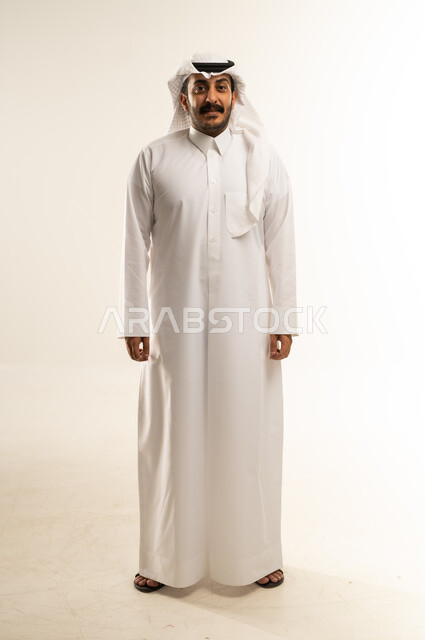 الوقوف باستعداد واستقامة، مفهوم الرجولة والثقة بالنفس، التقاط الصور الشخصية للوثائق الرسمية، بورتريه لشاب عربي خليجي قطري يرتدي الثوب التقليدي والغترة ينظر الكاميرا بتعابير البشاشة، الأناقة والاهتمام بالمظهر الخارجي، الطول الكامل للجسم، خلفية بيضاء