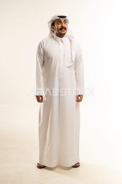 الوقوف باستعداد واستقامة، مفهوم الرجولة والثقة بالنفس، التقاط الصور الشخصية للوثائق الرسمية، بورتريه لشاب عربي خليجي قطري يرتدي الثوب التقليدي والغترة ينظر الى شيء ما بتعابير البشاشة، الأناقة والاهتمام بالمظهر الخارجي، الطول الكامل للجسم، خلفية بيضاء