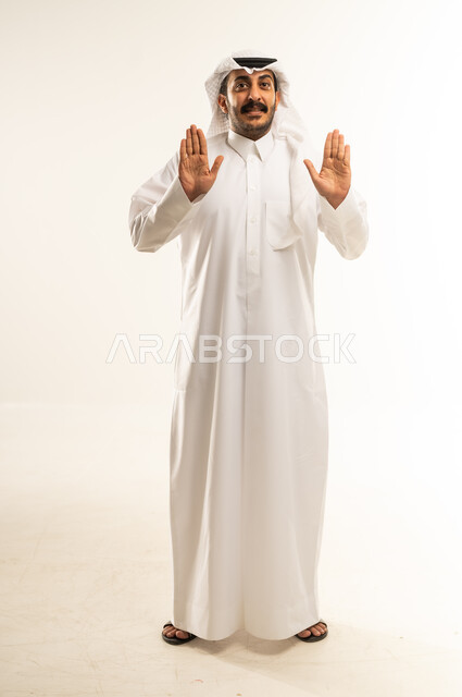 التحذير من فعل شيء ما، طلب التوقف وعدم الاقتراب, مفهوم الرفض والامتناع والانزعاج, بورتريه لرجل عربي خليجي قطري يرتدي الثوب والغترة يمد كفه نحو الأمام بإيماءات النهي عن فعل امر ما, الطول الكامل للجسم، خلفية بيضاء