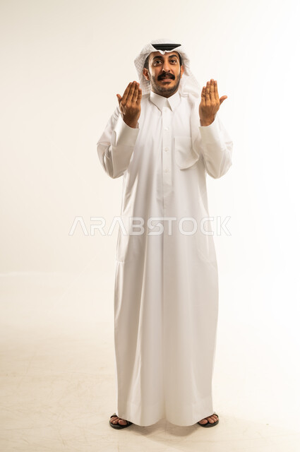 عرض ظاهرة الكف، النظر الى الكاميرا بايماءات السعادة والسرور، بورتريه لرجل عربي خليجي قطري مبتسم يرتدي الثوب التقليدي والشماغ يرفع كفيه مفتوحة للاعلى، مفهوم الاناقة والاهتمام بالمظهر الخارجي، الجسم بالطول الكامل، خلفية بيضاء