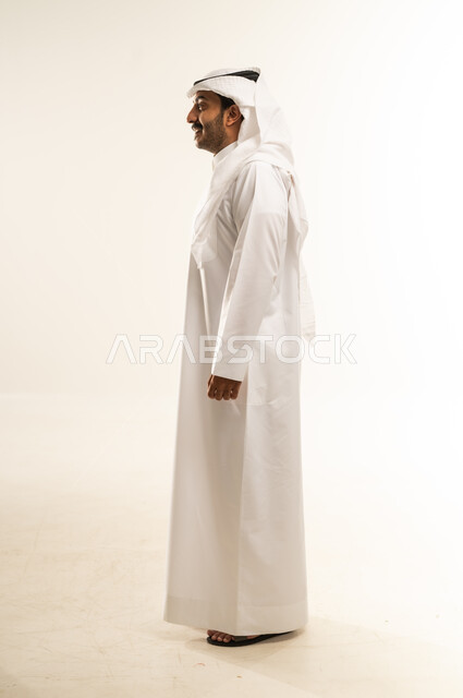 االنظر الى مكان ما بايماءات الثقة بالنفس، لاهتمام بالمظهر الخارجي, مفهوم الأناقة والرجولة, بورتريه من الجانب لرجل عربي خليجي قطري يرتدي الثوب التقليدي والغترة يقف باستقامة واعتدال, الجسم بالطول الكامل, خلفية بيضاء