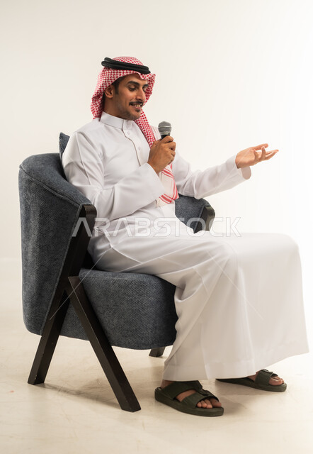 تسجيل المقاطع الصوتية والغنائية، إقامة الندوات وورش العمل والتحاور والنقاش مع الآخرين، إلقاء الخطابات والكلمات التوعوية، بورتريه من الجانب لشاب عربي خليجي بحريني يرتدي الثوب التقليدي والشماغ يجلس على كرسي ويمسك مكبر الصوت بيده، الطول الكامل للجسم، خلفية بيضاء