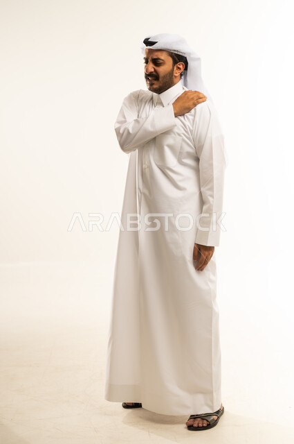 التهاب العضلات والمفاصل، الإحساس بالتعب والإرهاق, إيماءات الألم في الأكتاف، بورتريه لرجل عربي خليجي قطري يرتدي الثوب و الغترة يضع يده على كتفه بتعابير الوجع، الحاجه لوضع خطة علاجية, طلب المساعده للذهاب الى المستشفى، صورة الجسم بالطول الكامل، خلفية بيضاء