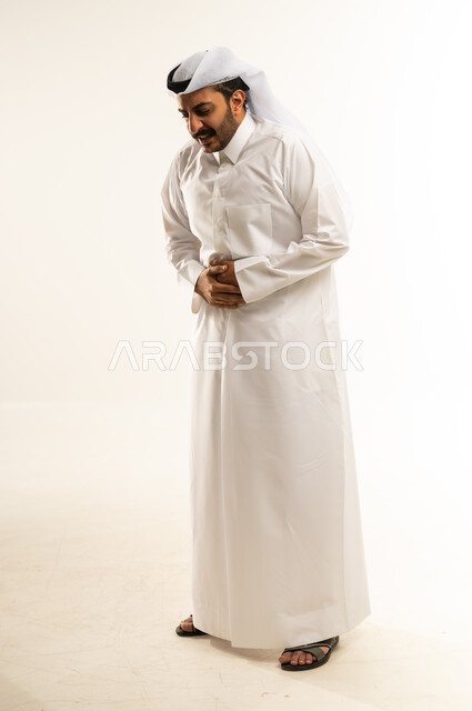 عسر الهضم والشعور بحرقة في المعدة، الحاجة للدواء ووضع خطة علاجية, الإحساس بالمغص و التعب والإرهاق, بورتريه لرجل عربي خليجي قطري يرتدي الثوب التقليدي والغترة يمسك بطنه بإيماءات الألم،  طلب المساعده للذهاب الى الطبيب، صورة الجسم بالطول الكامل، خلفية بيضاء